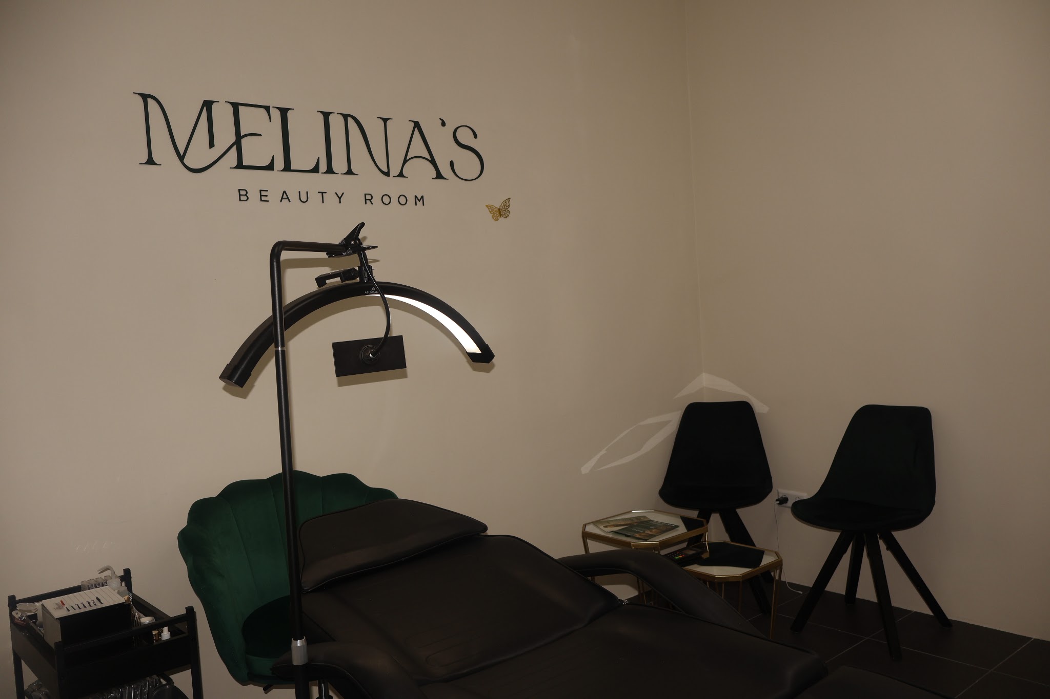 Behandelruimte met groene schelpstoel, ringlamp en het logo Melina’s Beauty Room op de muur